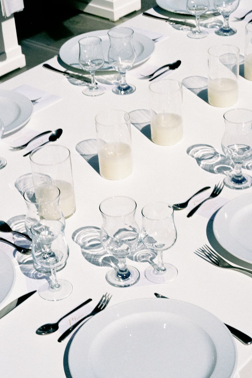 Elegant white wedding reception table set with crystal glassware, candles, and white plates.