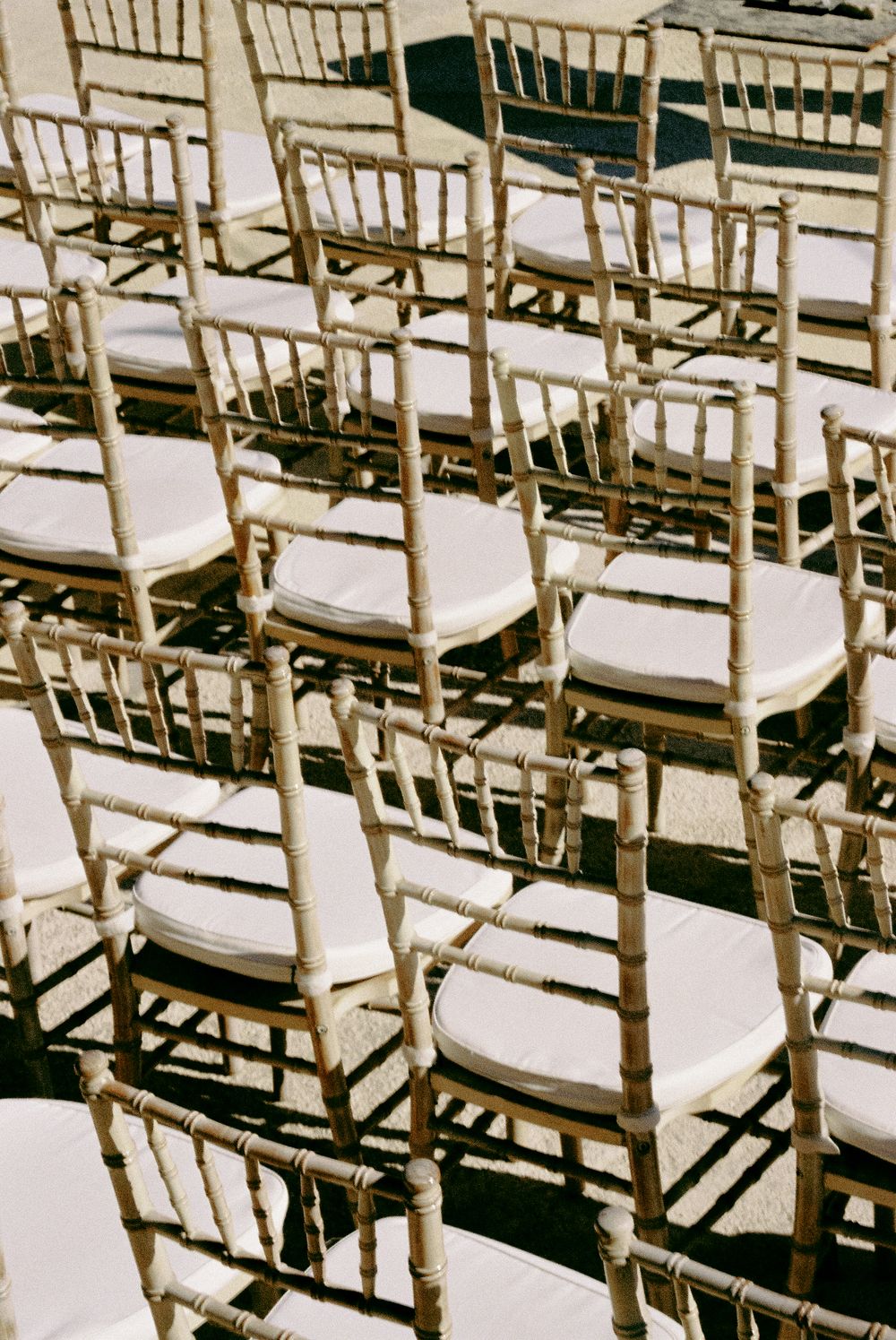 Rows of gold chiavari chairs with white cushions arranged for an outdoor wedding ceremony.