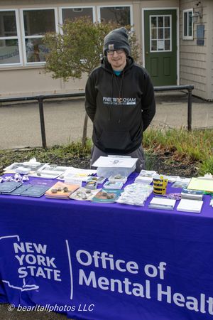 Person standing at New York State Office of Mental Health information table outdoors with brochures and resources.