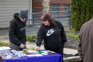 Two people in Nike hoodies browse items on a blue table at an outdoor vendor event.