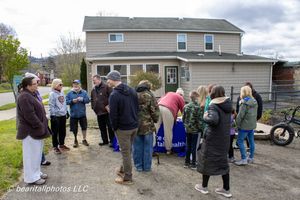 Group of people gathered outdoors near a house at a community health event on a cloudy day.
