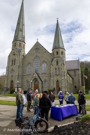 Group gathered at outdoor table near historic stone church with twin spires on cloudy day.