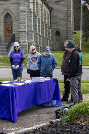 Group of volunteers gathered around a purple table outside a stone church during a community outdoor event.
