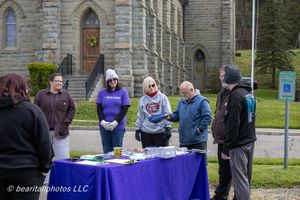 Group of people gathered around a purple table outdoors near a historic stone church during a community event.