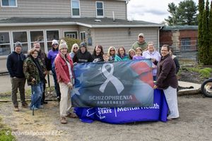 Group of people holding a Schizophrenia Awareness and Mental Health banner outdoors near a building.