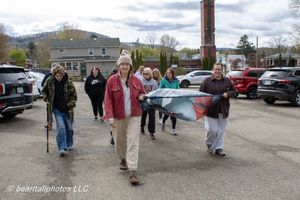Group of people walking through a parking lot on a cloudy day, led by a woman in a red jacket carrying artwork.