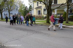 Group of people walking down a residential street lined with colorful houses on a cloudy day.