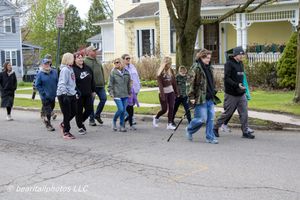 Group of people walking together on a residential street during a community walk event on a cloudy spring day.