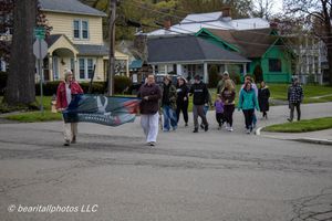 Group of people walking down a residential street during a community parade on a cloudy spring day.