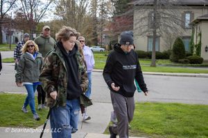 Group of people walking on a suburban sidewalk on a cloudy day, wearing casual jackets and hoodies.