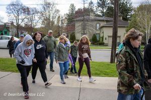 Group of people walking on a sidewalk in a suburban neighborhood on a cloudy day, wearing casual clothes.