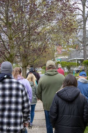 Group of people walking down a sidewalk lined with blooming spring trees in a residential neighborhood.