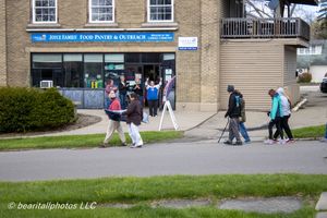 People walking past Joyce Family Food Pantry & Outreach brick building on a cloudy day.