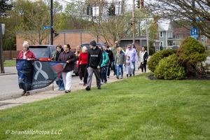 Group of people walking in a charity awareness walk, carrying a banner on a suburban sidewalk in spring.
