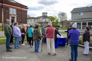 Group of people gathered outdoors near historic buildings on a cloudy day, attending a community event.