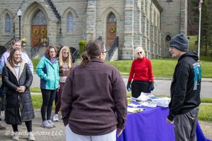 Group of people gathered outdoors near a table at a community event with a historic stone church in the background.