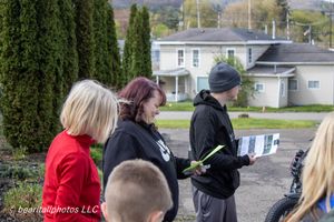 Group of people standing outdoors reviewing documents near residential homes on a cloudy day.