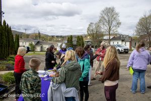 Group of people gathered outdoors at a community event on a cloudy day, standing around a table in a parking lot.