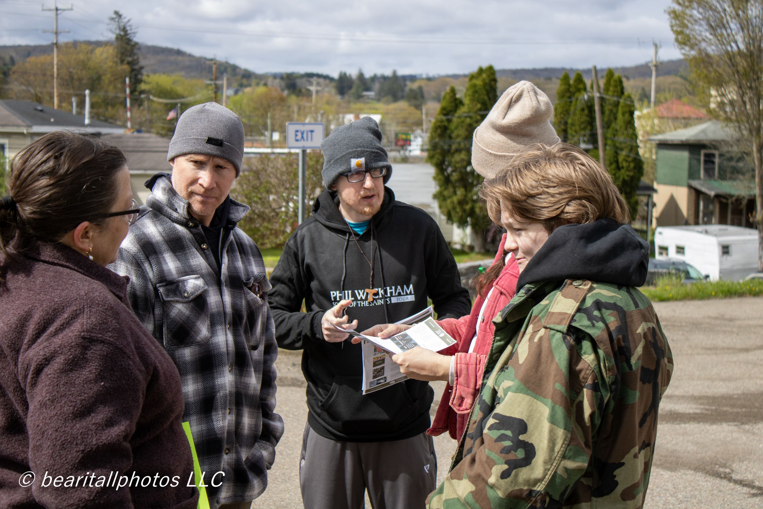 Group of four people outdoors reviewing printed materials on a cloudy day in a small town setting.