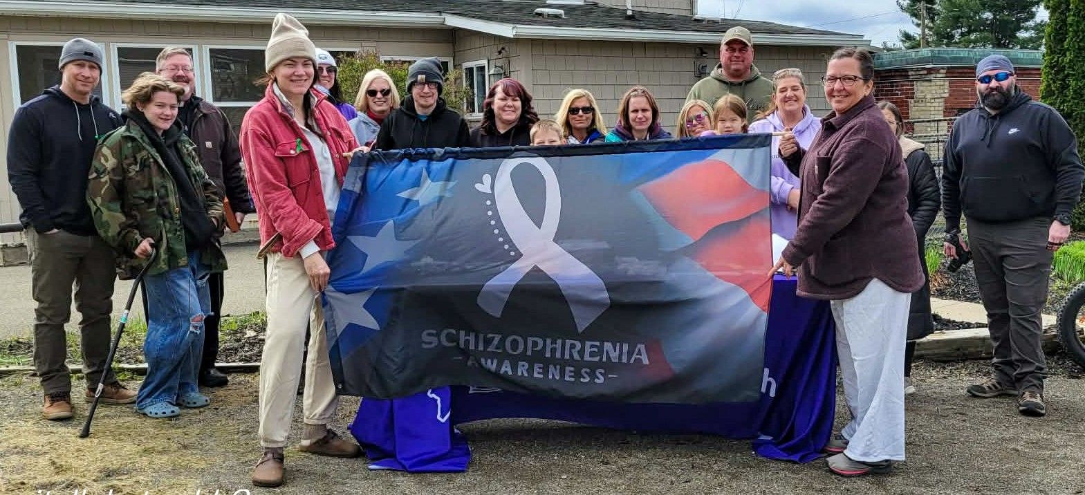 Group of people holding a Schizophrenia Awareness banner outdoors at a community awareness event.