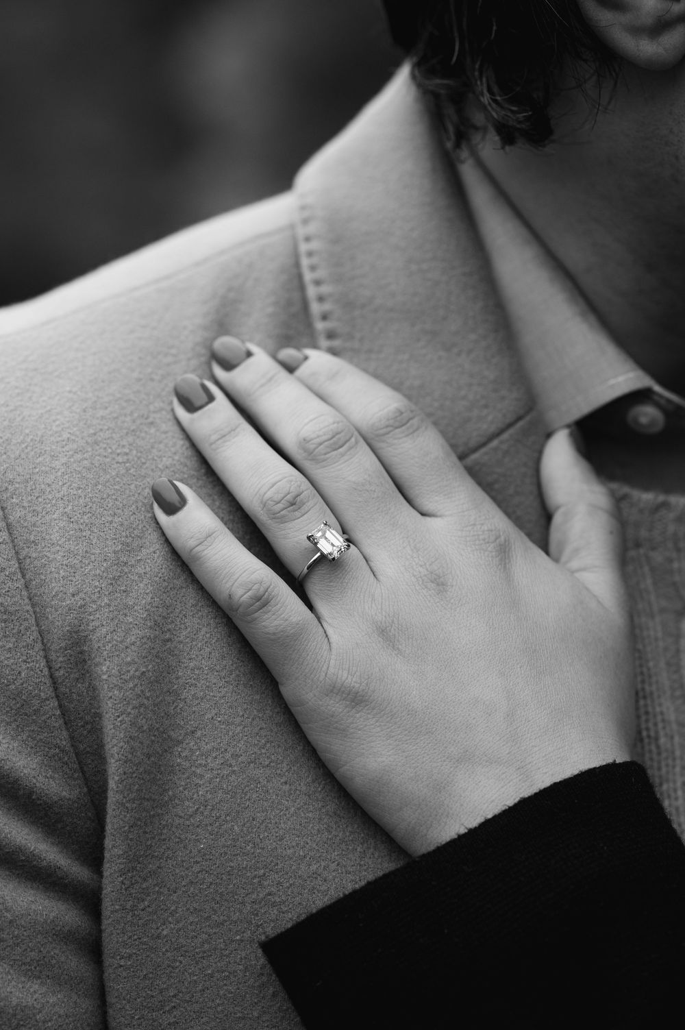 Close-up black and white photo of an engagement ring on a woman's hand resting on a man's chest.