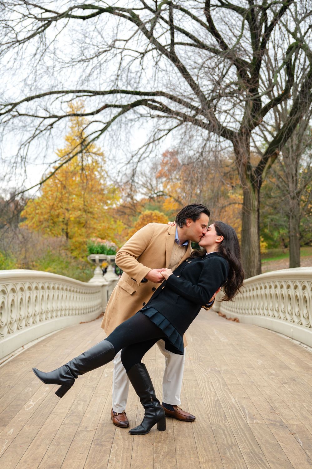 Couple sharing a romantic dip kiss on Bow Bridge in Central Park during autumn season.