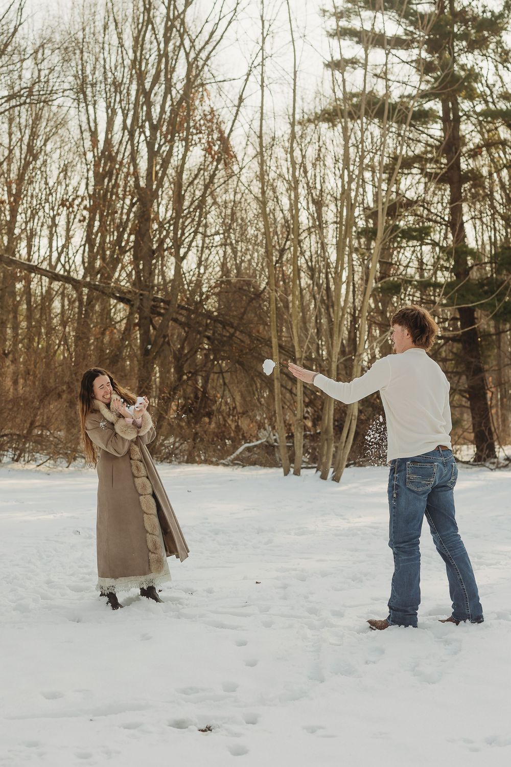 Couple playing in the snow, throwing snowballs in a winter forest setting.
