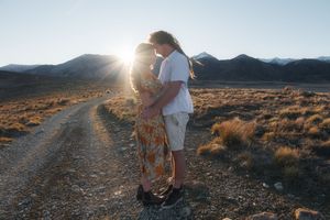 Couple embracing at sunset on a desert dirt road with mountains in the background.