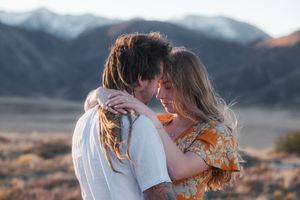 A couple embraces romantically outdoors with mountain landscape and golden sunset light in a desert setting.