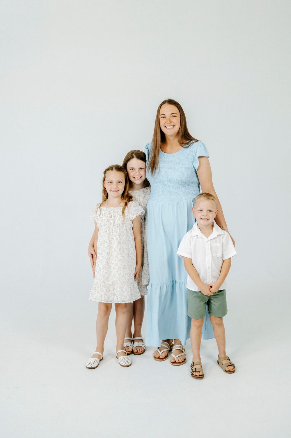 A smiling mother in a light blue dress poses with her three young children against a white background.