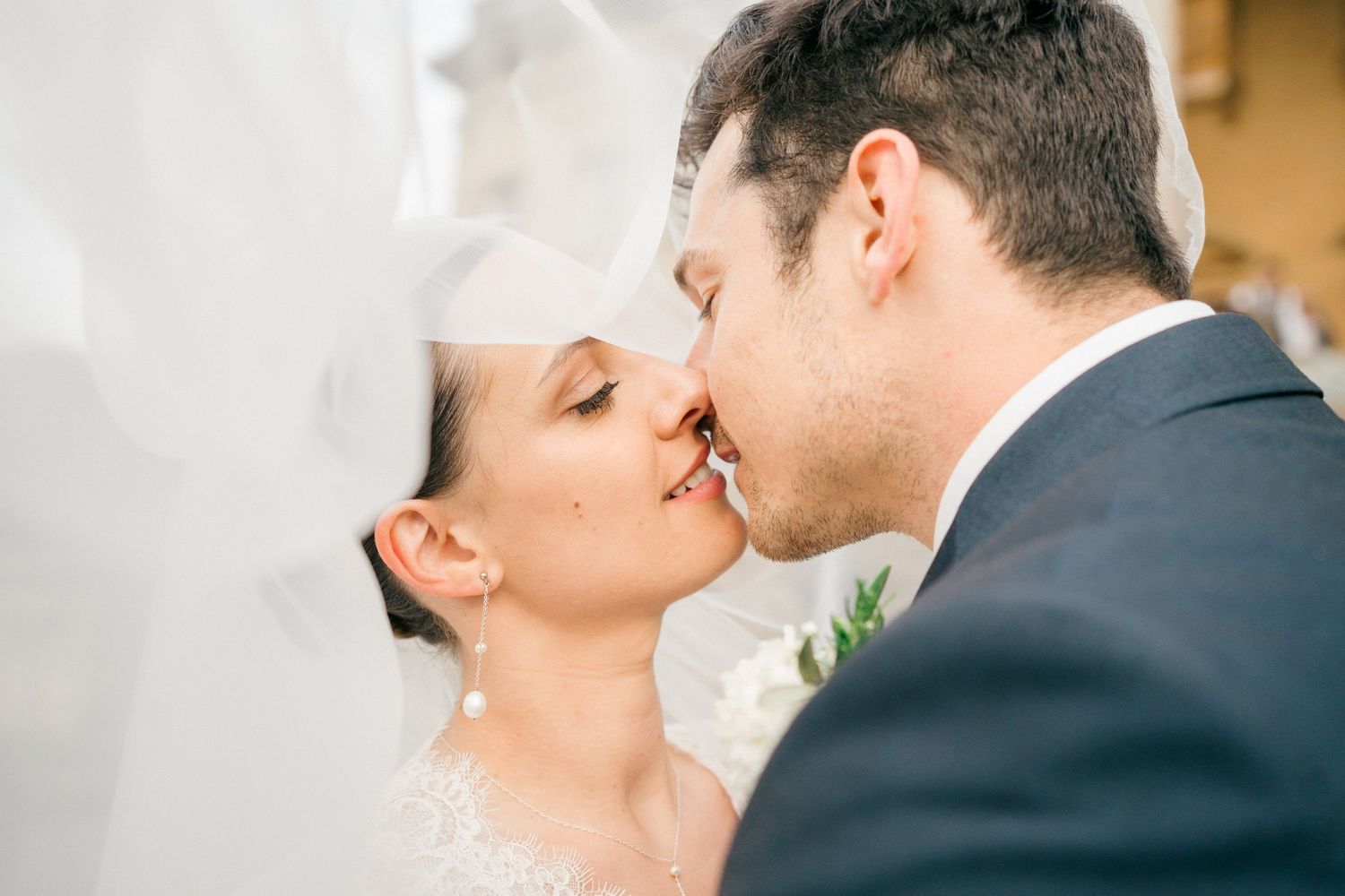 Bride and groom sharing a romantic kiss under a flowing white veil on their wedding day.