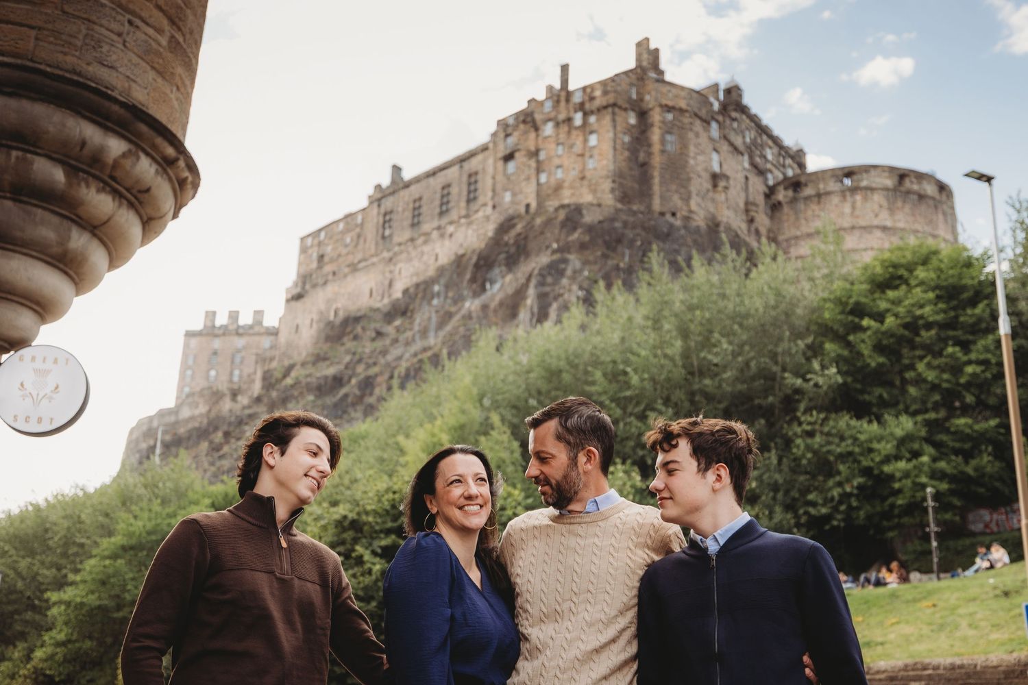 Four people smiling and conversing outdoors with Edinburgh Castle on a rocky hill in the background.