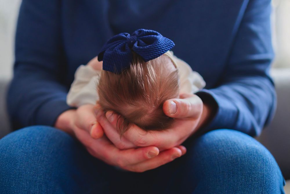 Adult cradling a newborn baby with a blue bow in their hands, close-up tender moment.