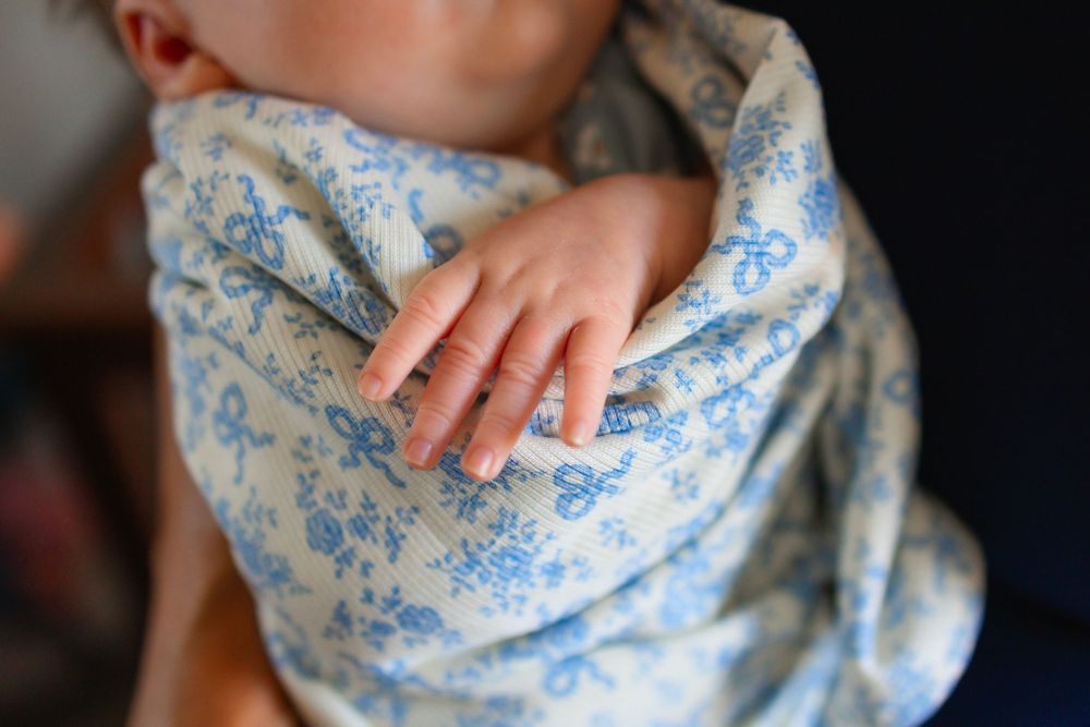 Close-up of a newborn baby wrapped in a blue and white floral swaddle blanket with tiny hand visible.
