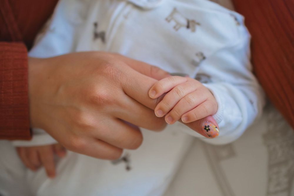 Close-up of a mother holding her newborn baby's tiny hand, wearing a white onesie with animal prints.