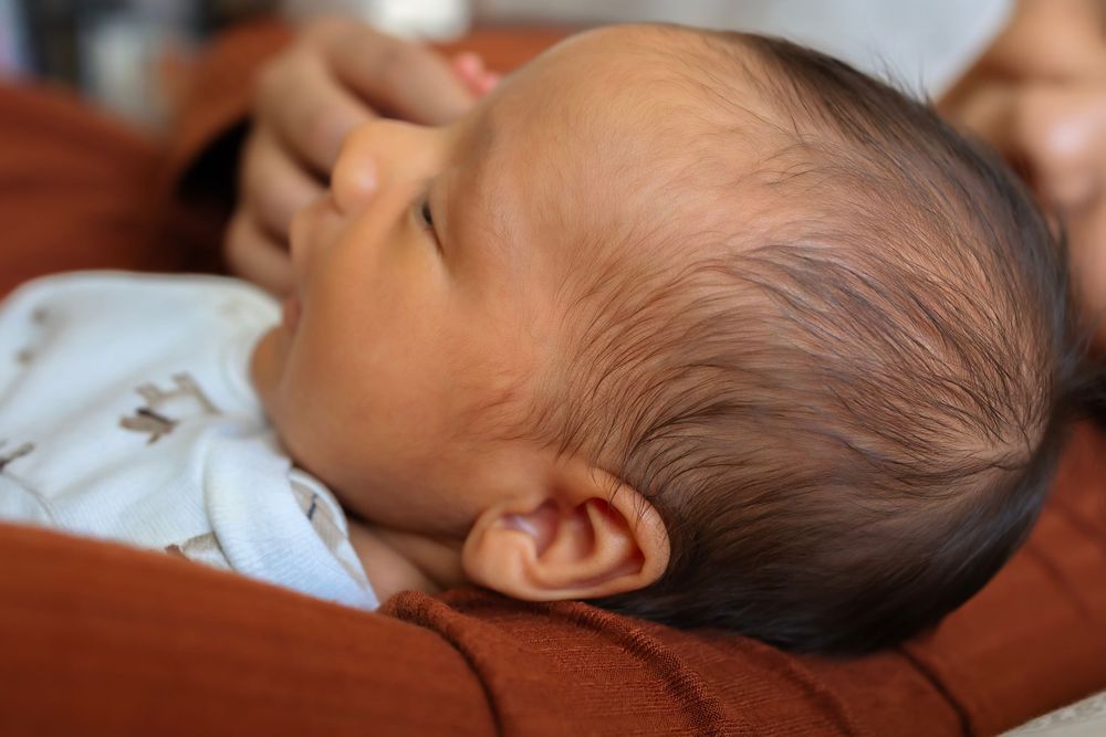 Peaceful newborn baby sleeping on a caregiver's chest, with soft dark hair and delicate features visible.
