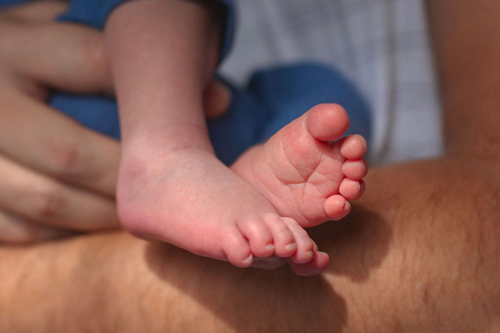 Close-up of tiny newborn baby feet resting on an adult's lap in warm sunlight.