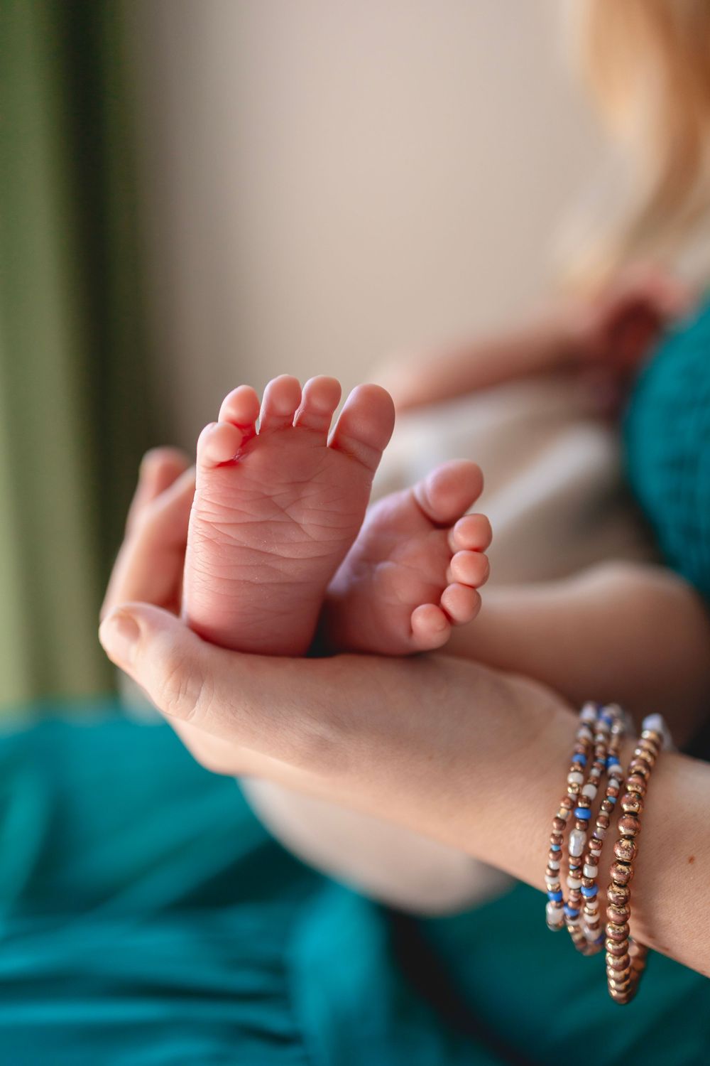 Close-up of a mother's hands holding tiny newborn baby feet, wearing colorful beaded bracelets.
