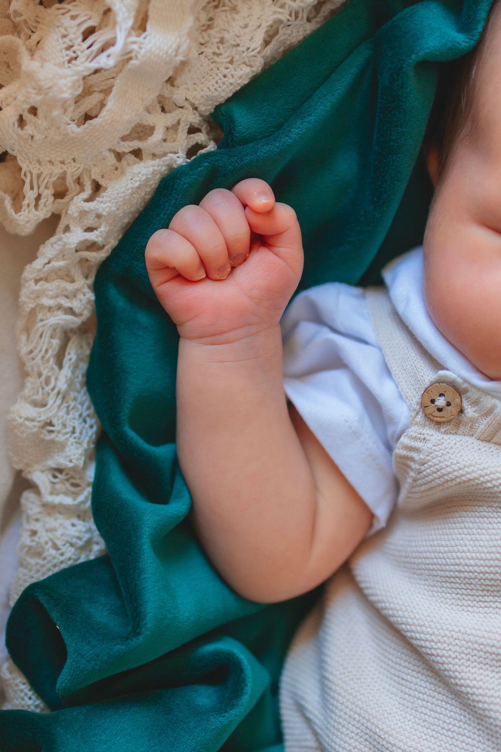 Close-up of a sleeping baby's tiny clenched fist resting on a teal and cream knit blanket.