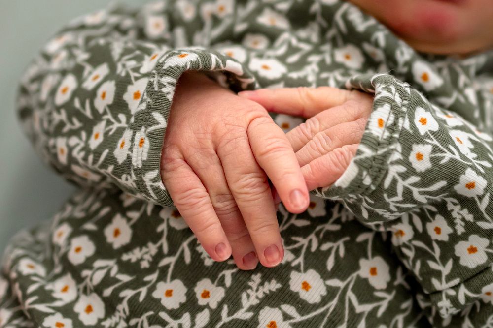 Close-up of a newborn baby's tiny hands resting on a floral green and white onesie.