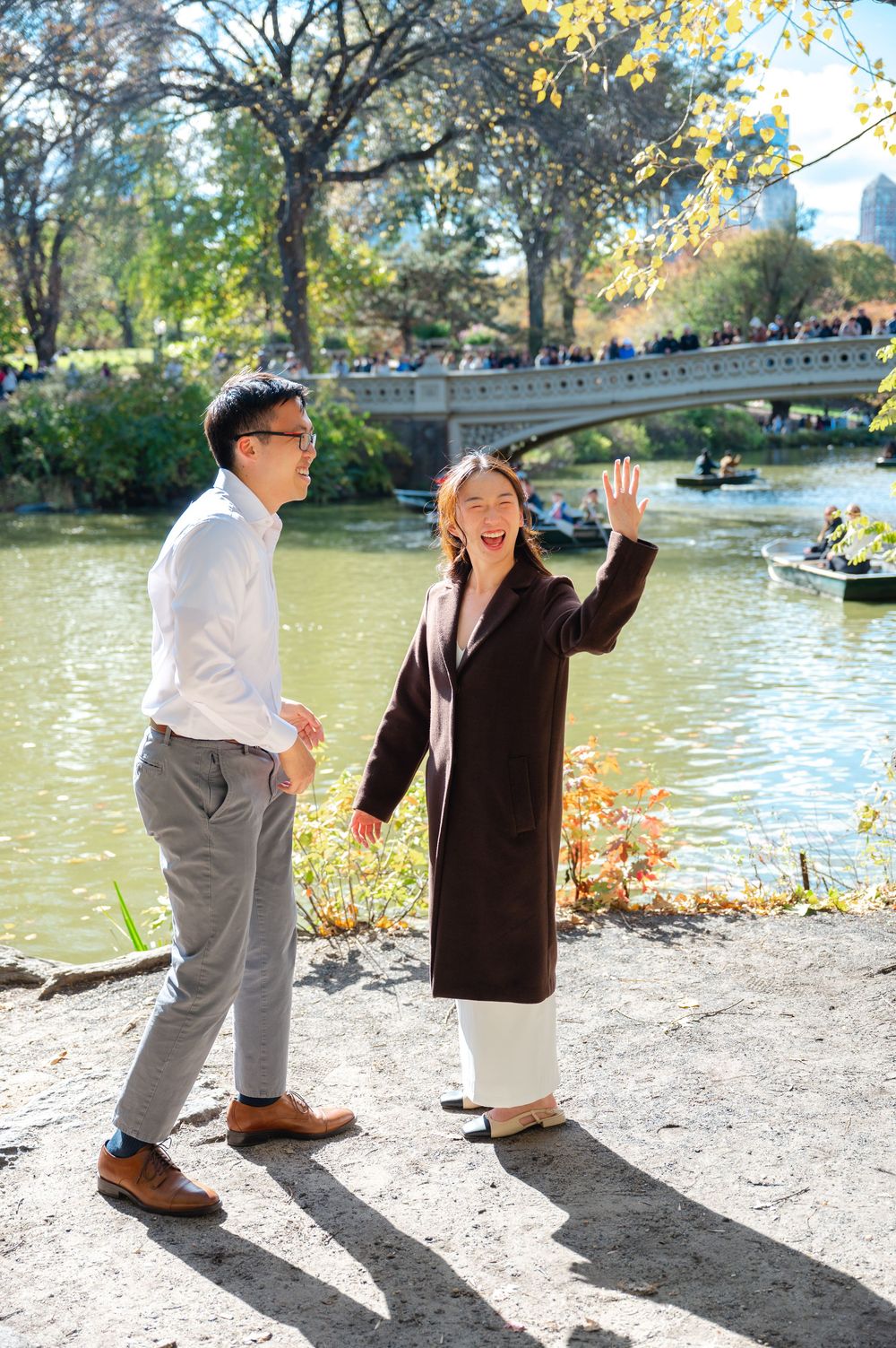 Joyful couple walking and laughing together along Central Park lake with Bow Bridge.