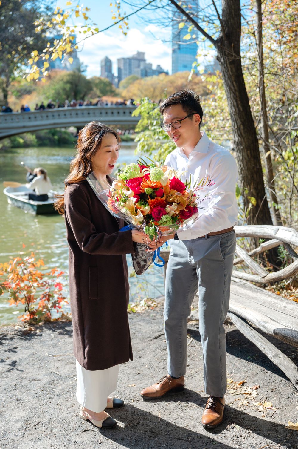 Man presenting colorful bouquet to woman near Central Park lake on sunny autumn day.