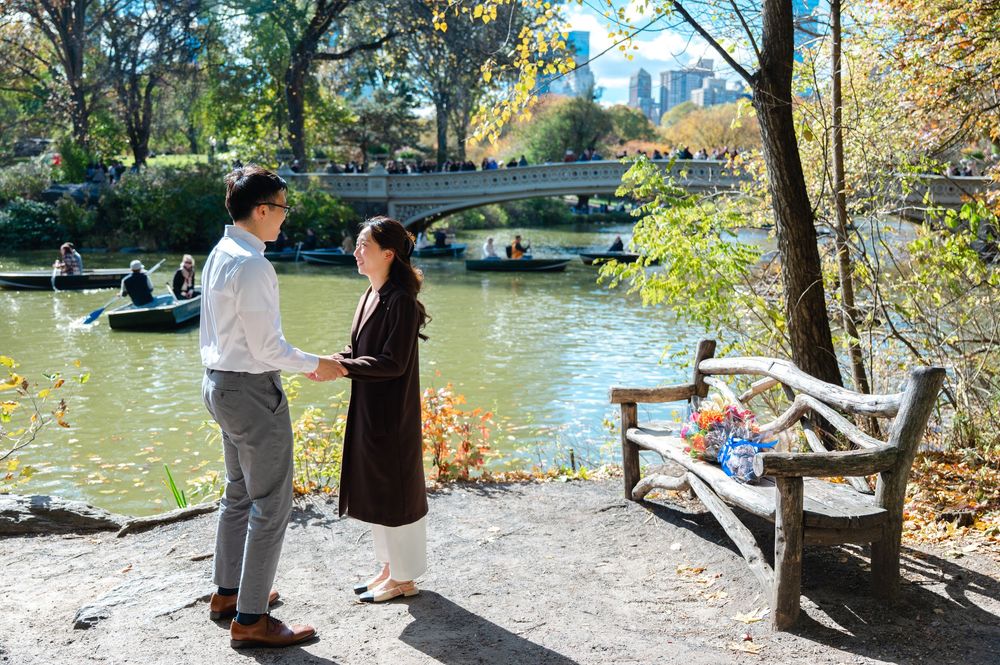 Couple exchanging vows by Central Park lake with rowboats, surrounded by autumn trees and city skyline.