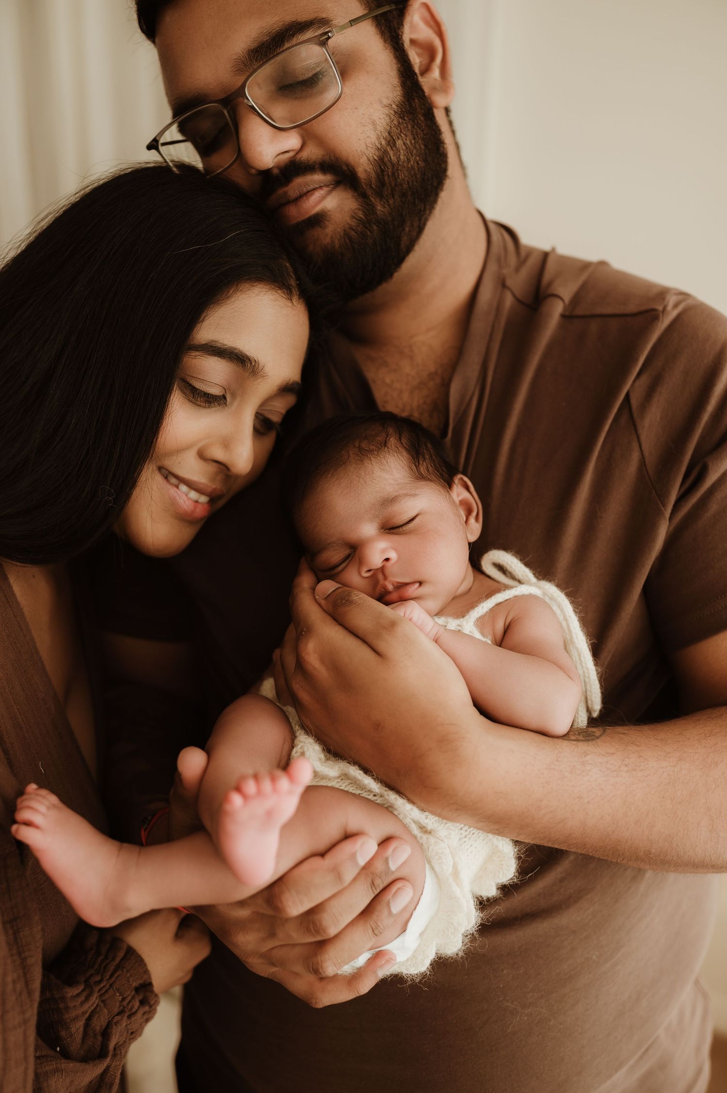 A couple tenderly holds their sleeping newborn baby, sharing a warm family moment in soft natural light.