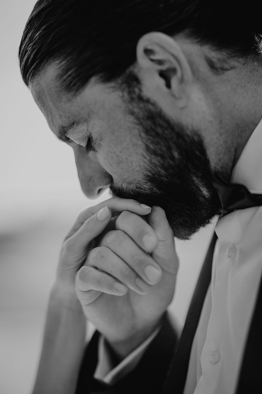 Black and white close-up of bearded groom in bow tie with clasped hands.