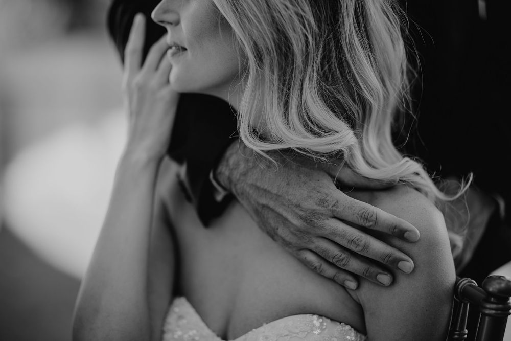 Black and white photo of a bride with blonde hair, a hand gently resting on her shoulder.