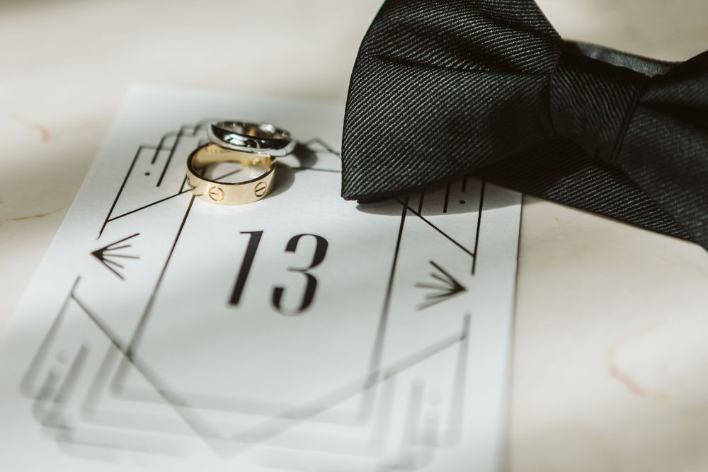 Black bow tie and gold wedding rings resting on a table number 13 card for an elegant wedding reception.