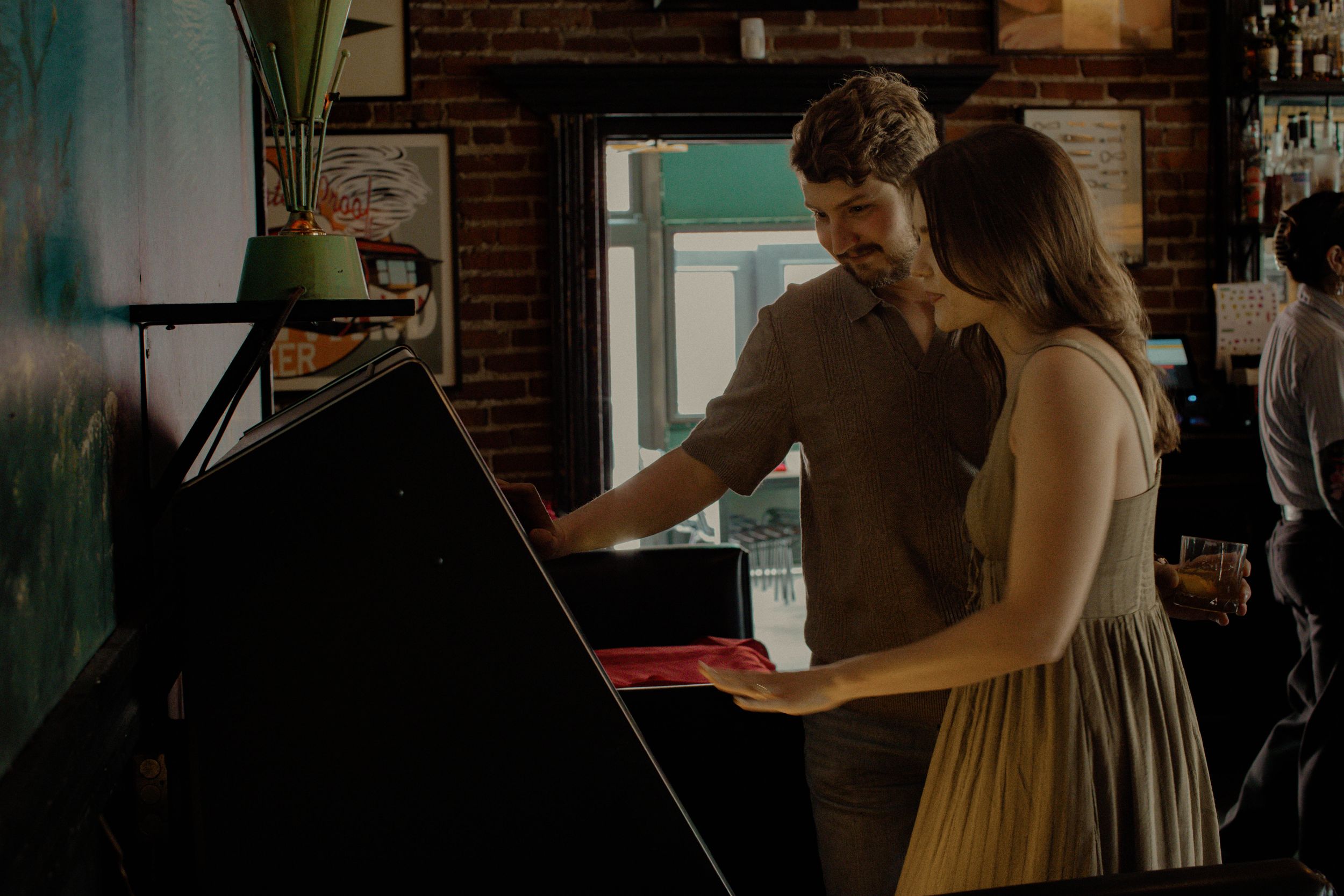 A man and woman stand in front of a jukebox looking at the song selection during their Kansas City engagement photo session.