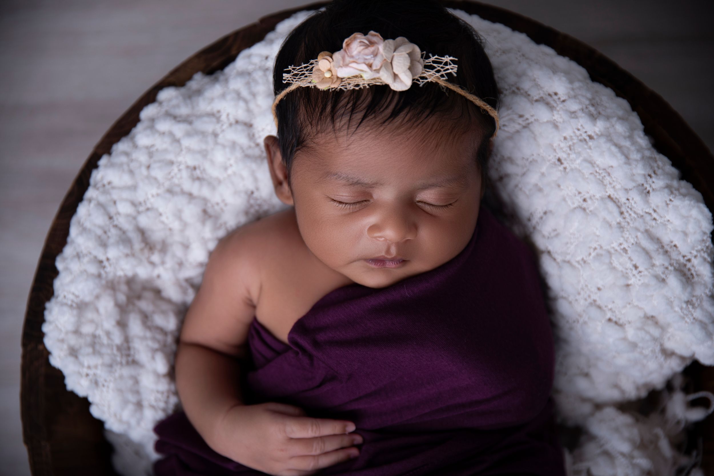 beautiful baby girl sleeping in a wooden bucket with a white blanket and a purple wrap in our Pacific pines newborn studio