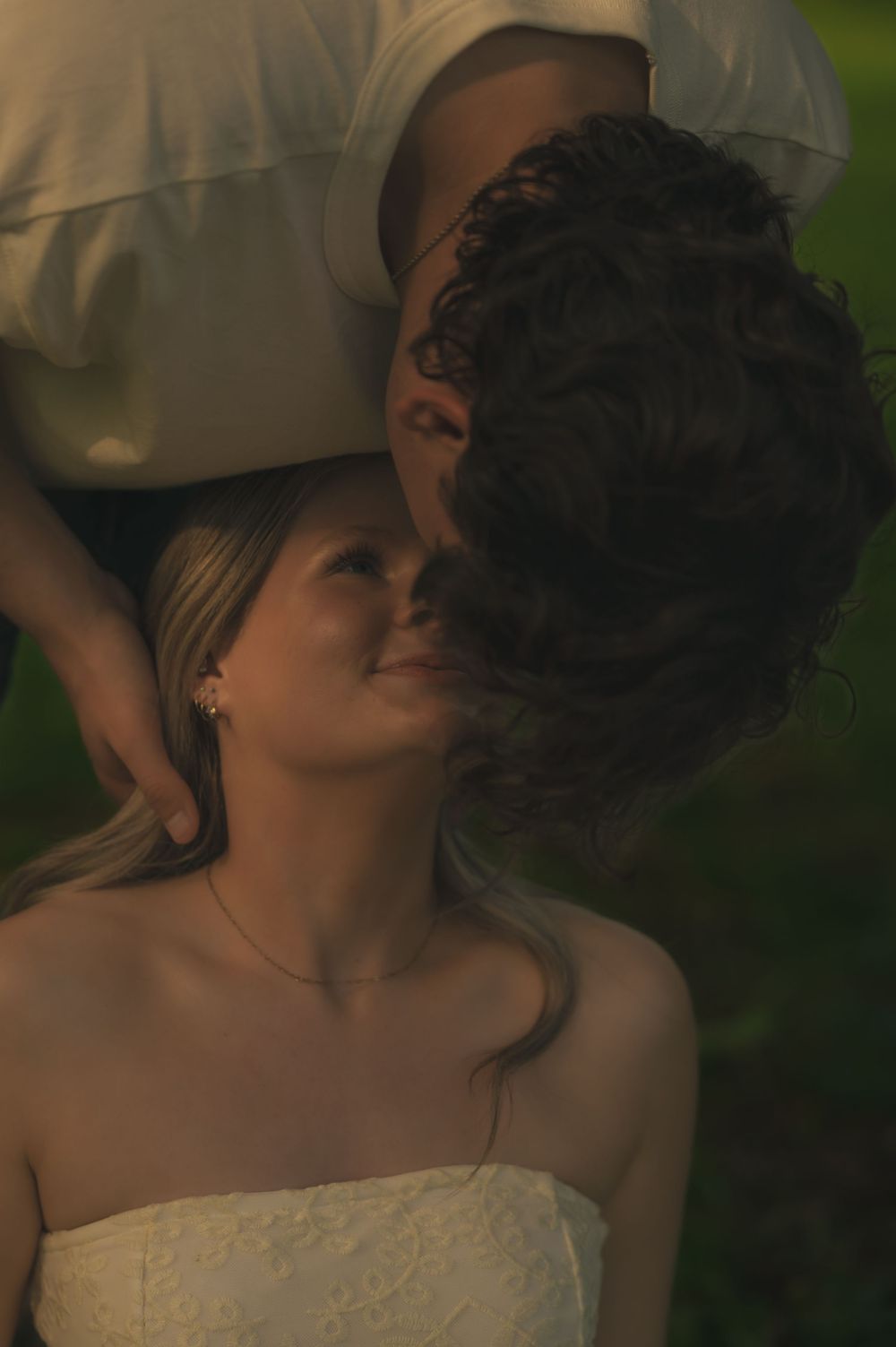 Groom tenderly kissing the forehead of his smiling bride in warm golden hour light outdoors.